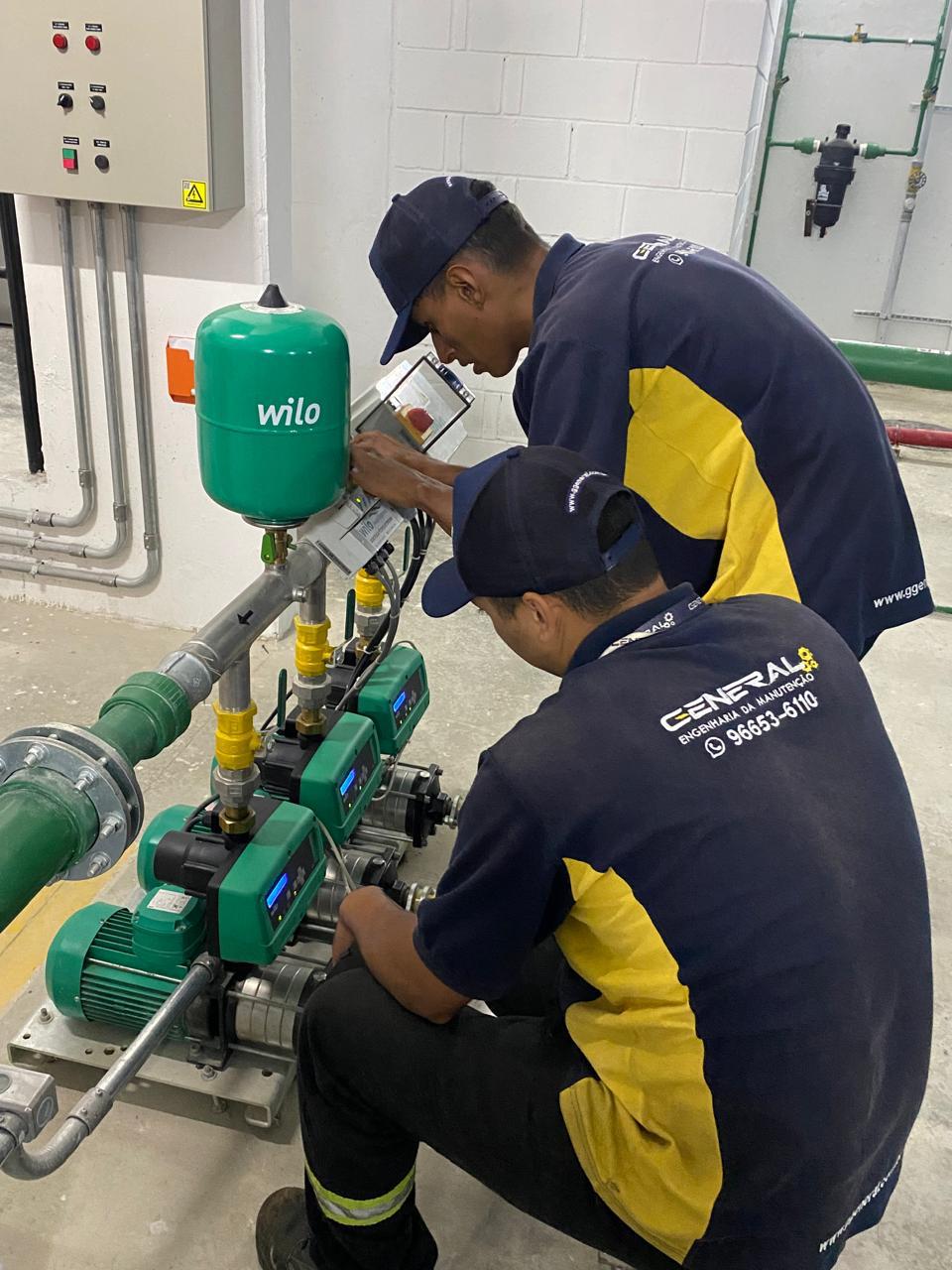 Dois técnicos da General, de uniforme azul-marinho e amarelo, em manutenção de um conjunto de pressurização numa casa de máquinas